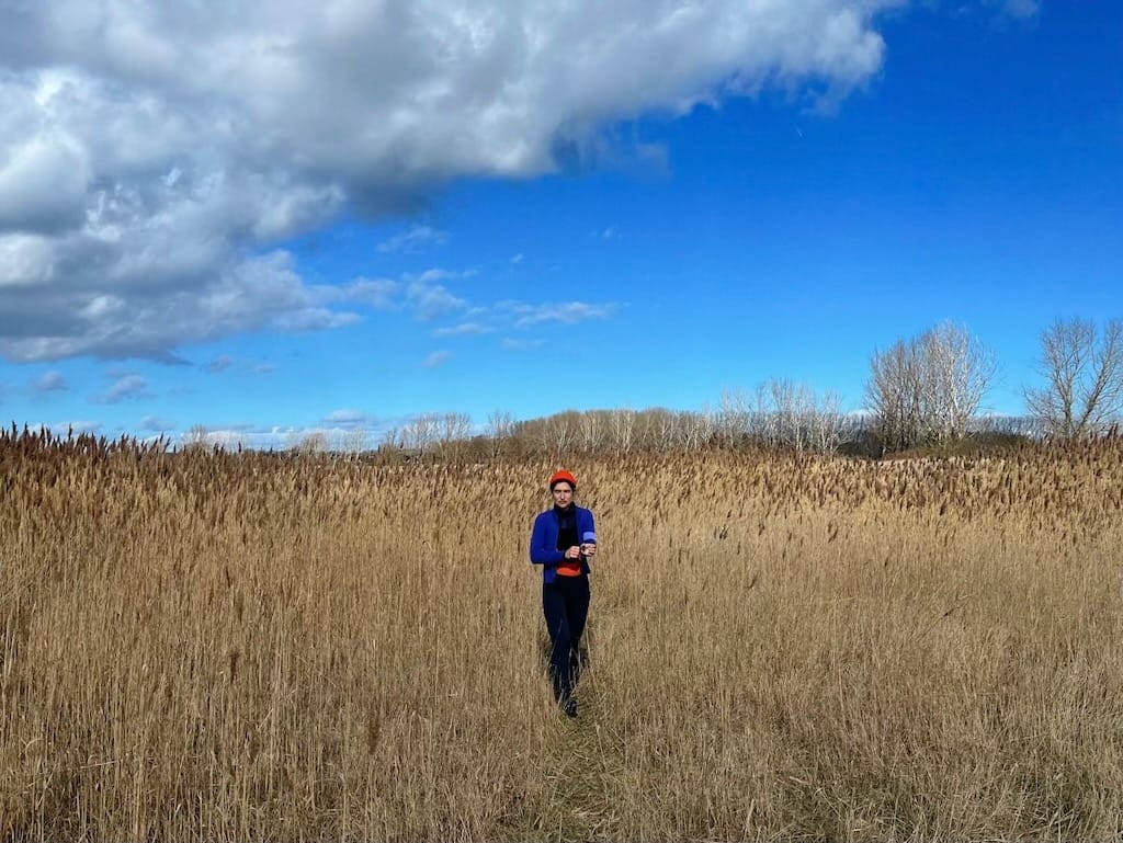Stephanie wearing winter lycra and a tiny red beanie in a wintery field along the coast of the Baltic Sea