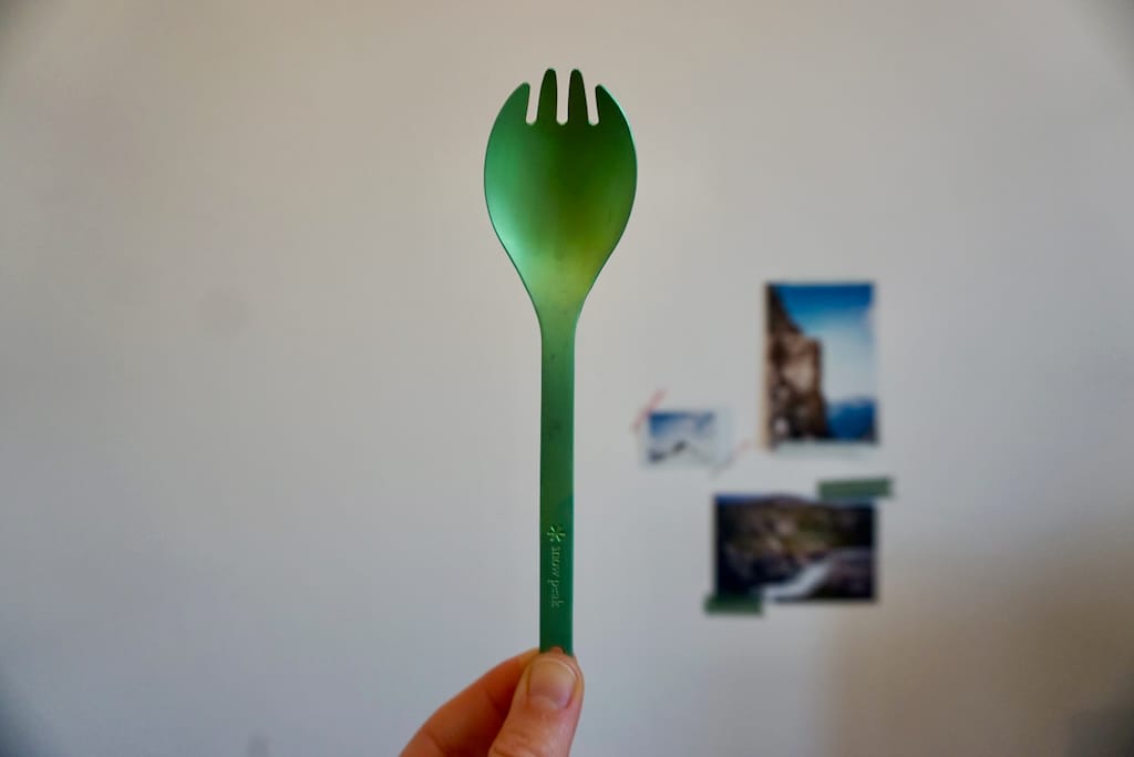 Two fingers holding a green Snow Peak spork in front of a white wall